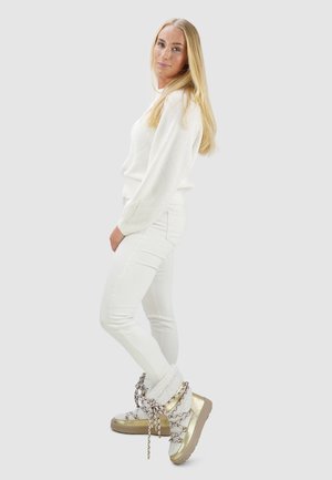 Witte gebreide trui, witte strakke jeans en crème- en goudkleurige plateaulaarzen met kettaccenten en pluizige details.