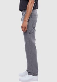 Pantalones de mezclilla gris con un corte relajado, que cuentan con bolsillos laterales y un diseño de pierna recta. Combinados con zapatillas deportivas blancas.