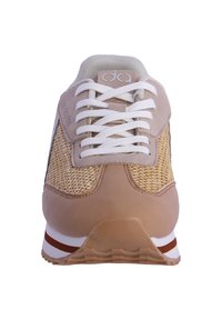 Zapatilla beige con textura trenzada en la parte superior, cordones blancos y cuello acolchado. Presenta una suela estratificada con rayas marrones y blancas.