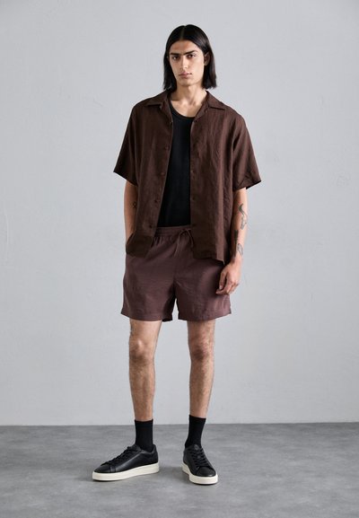 Brun kortermet skjorte med knapper, svart tanktop, brune shorts og sorte joggesko med hvite såler; glatt stoff og løs passform.