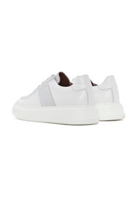 Baskets blanches en cuir avec une texture lisse, présentant un panneau latéral gris et une épaisse semelle en caoutchouc blanc. Design minimaliste avec un bout arrondi.