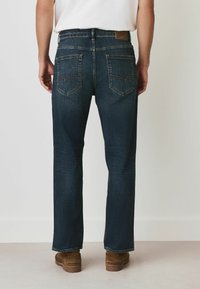 Mörkblå denimjeans med rak passform, med två bakfickor, brun skinnapplikation och subtila sömnadsdetaljer. Kombinerat med ljusbruna skor.