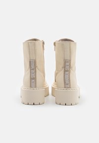 Bottes de cheville en cuir beige avec une finition texturée, fermeture zippée et accents de logo blanc sur les côtés. Semelle en caoutchouc épaisse et col rembourré.