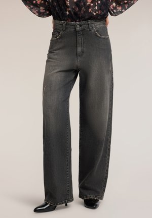 Schwarze Jeans mit hohem Bund und weitem Bein, leicht ausgewaschen, kombiniert mit schwarzen spitzen Schuhen und einer dunklen, geblümten Bluse.
