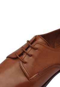Brown leather dress shoe with a smooth texture, rounded toe, and three eyelets for lace closure. Slightly raised stitching details visible.