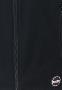 Giacca nera con zip centrale, texture liscia e patch rotondo con "COLMAR" in bianco su uno sfondo scuro.