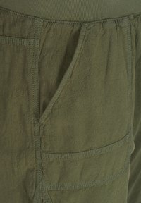 Gros plan sur un pantalon en tissu vert olive montrant une ceinture élastique et une grande poche avant avec des coutures visibles.