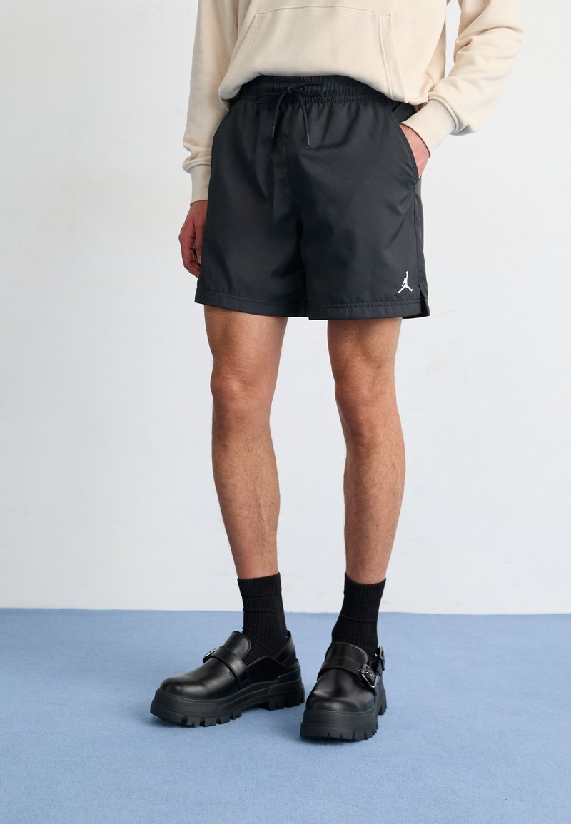 Black shorts with an elastic waistband and drawstring, featuring a white Jordan logo. Worn with chunky black shoes and black socks.