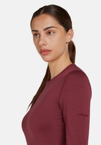 Maglia a maniche lunghe color bordeaux realizzata in un tessuto a maglia testurizzato. Presenta un colletto rotondo e un logo sulla manica sinistra.