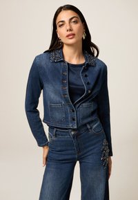 Veste en denim avec col en perles, poches avant et fermeture à boutons. Accompagnée d'un jean taille haute assorti avec des embellissements détaillés.