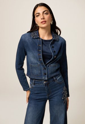Jeansjacke mit besticktem Kragen, Vorderentaschen und Knopfverschluss. Begleitet von passenden hoch taillierten Jeans mit detaillierten Verzierungen.