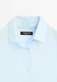 Camicia azzurra chiaro con colletto classico, maniche corte e tessuto testurizzato. Etichetta con la scritta "Massimo Dutti" attaccata all'interno.