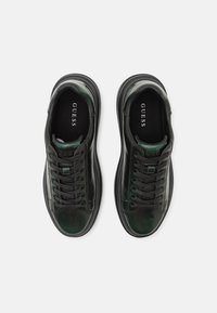 Sneaker in pelle nera e verde con una superficie liscia, punta rotonda, design con lacci e logo "GUESS" sulla linguetta e sulla soletta.