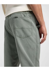 Vaaleanvihreät puuvillasekoitehousut, joissa on rento istuvuus, takataskut ja vaaleanruskea ommelviimeistely. Brändilogo vyötäröllä.