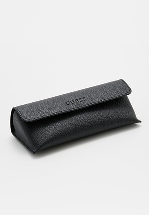 Custodia per occhiali in pelle nera strutturata con chiusura a patta e logo "GUESS" impresso sul davanti.