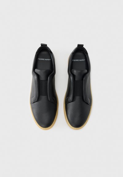 Μαύρα δερμάτινα παπούτσια χωρίς κορδόνια με ελαστικές ταινίες, υφή στην επιφάνεια και μπεζ ελαστική σόλα. Φέρουν λογότυπο στη σόλα του ποδιού.