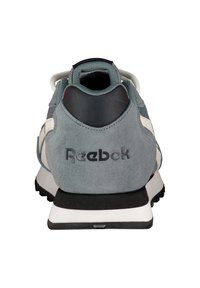 Zapatillas de ante gris con acentos negros, talón texturizado y suela blanca. Presenta el logo "Reebok" en la parte trasera y un collar acolchado.