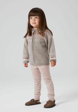 Cardigan grigio lavorato a maglia con motivo bianco, chiusura con zip e bottoni in legno marroni; abbinato a pantaloni a coste rosa chiaro e scarpe in suede marroni.