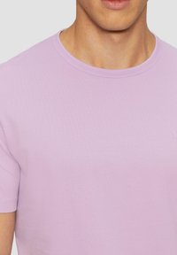 Vaaleanvioletti puuvillapaita, jossa on pyöreä kaula-aukko, lyhyet hihat ja huomaamaton brändäys rintavarustuksessa. Silkkinen pinta ja istuva muotoilu.
