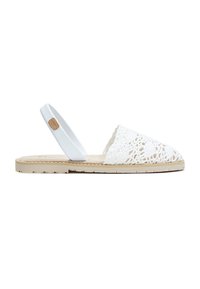 Sandalia plana con suela beige, cubierta de dedos en ganchillo blanco y tira trasera blanca con una pequeña etiqueta marrón.