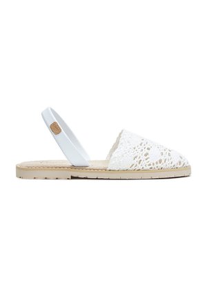 Sandalia plana con suela beige, cubierta de dedos en ganchillo blanco y tira trasera blanca con una pequeña etiqueta marrón.