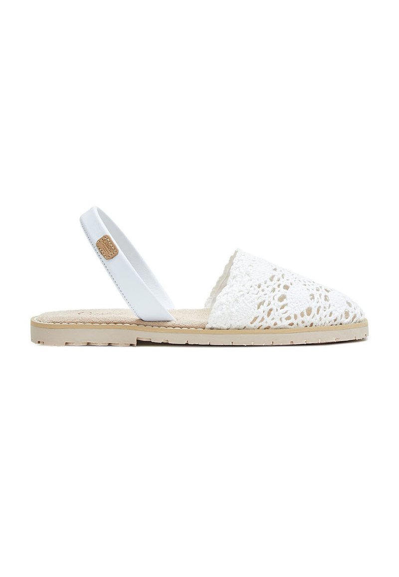 Sandalia plana con suela beige, cubierta de dedos en ganchillo blanco y tira trasera blanca con una pequeña etiqueta marrón.
