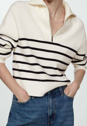 Crème rib gebreid pullover met een halve ritssluiting kraag. Bevat zwarte horizontale strepen. Gecombineerd met high-waisted blauwe denim jeans.