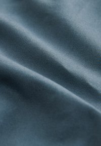 Tejido textil en azul, con una textura suave y un sutil patrón de acanalado diagonal, que refleja una luz suave a través de pliegues delicados.