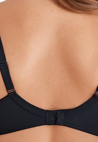 Sustainabile in tessuto morbido, reggiseno nero con spalline regolabili e chiusura con gancetti. Vista dal retro, tonalità della pelle visibile.