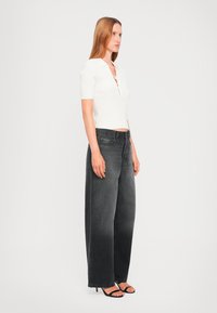 White ribbed short-sleeve top with a collar, paired with high-waisted loose-fit black jeans and black strappy heels. Clear design lines.