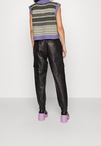 Gestricktes ärmelloses Oberteil in Creme und Schwarz mit lila Kragen, kombiniert mit schwarzen Leder-Cargohosen und lavendelfarbenen klobigen Absätzen.