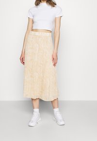 Gul plisserad midikjol med ett subtilt marmormönster, kombinerad med en vit kort t-shirt och vita sneakers.