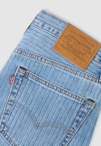 Jean Levi's en denim bleu clair montrant la poche arrière, l'étiquette rouge Levi's et la pièce en cuir beige de la marque avec le logo et le texte de qualité.