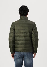 Polstret grønn jakke med høy krage, med et quiltet design og lett tekstur. Brukt over blå jeans.