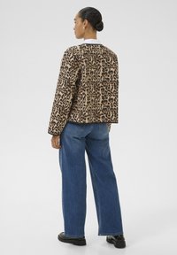 Veste à imprimé léopard avec une coupe décontractée et des manches longues, associée à un jean bleu à jambe large et des chaussures noires. Détail de col de chemise blanche visible.