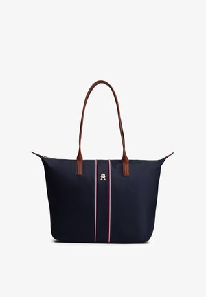 Navy blue tote bag with brown leather handles, vertical red and white stripes, and gold logo detail centered on front.