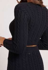 Schwarzer kabelgestrickter Pullover mit einem cropped Design, langen Ärmeln und geripptem Saum. Die Textur weist erhabene Muster auf dem Stoff auf.