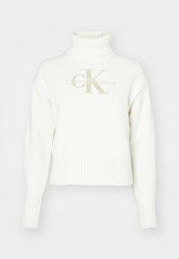 Hvit strikket høyhalset genser med ribbestrikkede mansjetter og kant. Har et beige "CK"-logo og tekst "Calvin Klein Jeans" i matchende farge.