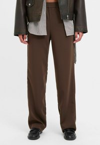 Brūni, platajā kāju bikses, kas izgatavotas no gludas, vieglas auduma ar elastīgu jostu. Kombinētas ar melnu ādas jaku.