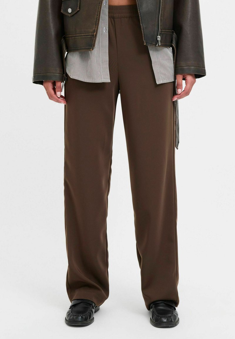 Brūni, platajā kāju bikses, kas izgatavotas no gludas, vieglas auduma ar elastīgu jostu. Kombinētas ar melnu ādas jaku.