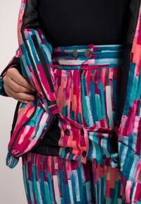 Giacca imbottita colorata con un motivo a pennellate multicolori in rosa, blu e bianco, dotata di doppi bottoni a pressione e dettagli con cerniera.