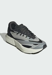 Atletická teniska s textúrovaným zvrškom v čiernej a sivej farbe, so silnou bielou medzičlánkovou časťou a čiernou podrážkou. Systém šnurovania s polstrovaným golierom.