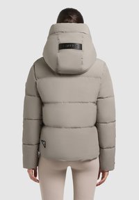 Veste matelassée de couleur gris clair, avec une capuche, des accents côtelés et un logo au dos. Design texturé et rembourré avec des coutures horizontales.