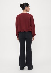 Sudadera amplia color burdeos con escote redondeado, combinada con jeans negros de campana. El conjunto incluye calzado negro grueso.