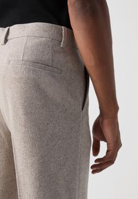 Gray wool trousers featuring a tailored fit, a flat back pocket, and subtle texture, paired with a black waistband.