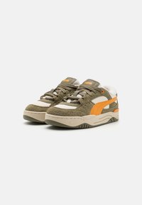 Sneaker in suede verde con accenti arancioni, dotati di pannelli testurizzati, suola beige e lacci. Include un logo sulla linguetta.