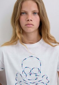 Weißes Baumwoll-T-Shirt mit buntem gesticktem Skull-und-Kreuzbones-Design. Kurzärmlig mit mehrfarbigen Akzentstreifen. Glatte Textur.