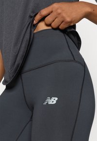 Leggings noires ajustées avec une texture lisse et des coutures contrastantes. Présente un petit logo réfléchissant sur la jambe inférieure.