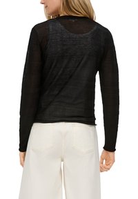 Schwarzes Langarmoberteil mit einem strukturierten, durchsichtigen Design, runder Halslinie und geradem Saum, kombiniert mit hellen weitem Hosen.