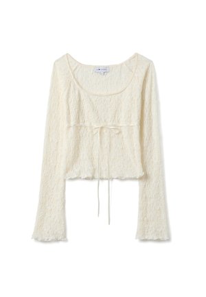 Top corto de encaje crema con mangas largas, escote en forma de U y detalle de lazo delantero, con un delicado patrón floral y puños ligeramente acampanados.